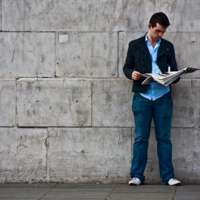 A man reads a newspaper by the wall.